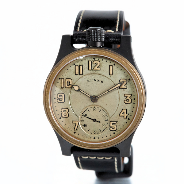 A vintage-style wristwatch with a black strap, black case, and a warm beige dial featuring black Arabic numerals and a small subdial at the 6 o'clock position.