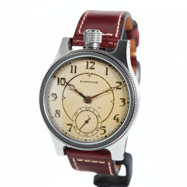 A vintage-style wristwatch with a silver-toned metal case, a cream-colored dial with black Arabic numerals, and a reddish-brown leather strap with white stitching, shown against a plain white background.