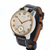 A vintage wristwatch with a round silver-toned case, gold-tone bezel and hands, a cream-colored dial with black Arabic numerals, and a black leather strap with white stitching and a brown interior lining, shown on a plain white background.