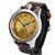 A vintage-style wristwatch with a round silver-tone case, a textured gold dial featuring black Arabic numerals and hands, and a dark brown leather strap, shown on a plain white background.