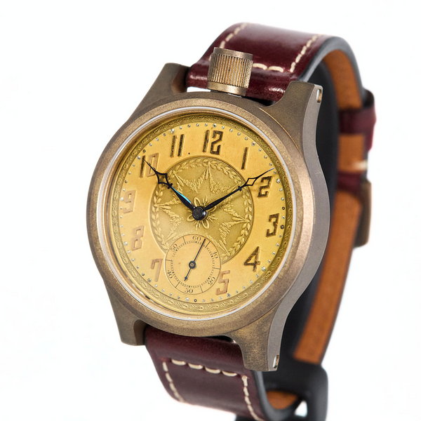 A vintage-style wristwatch with a round bronze-toned case, a gold dial featuring a central floral emblem and black Arabic numerals, and a dark brown leather strap with white stitching.