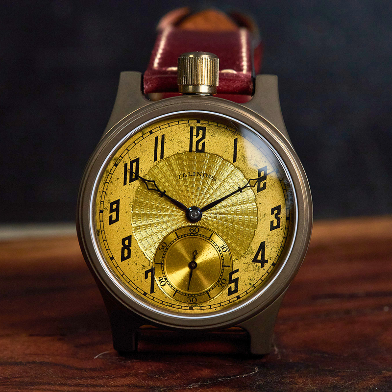A vintage-style wristwatch with a round bronze-toned case, a textured gold dial with black Arabic numerals, and a dark reddish-brown leather strap, resting on a wooden surface against a dark background.