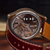 Close-up of a mechanical watch with a transparent dial showing intricate gears and a brown leather strap on a wooden surface.