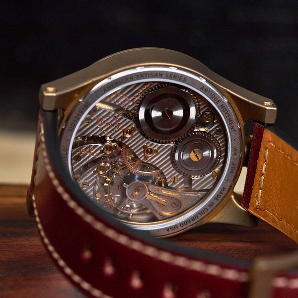 Close-up of a mechanical watch with a transparent dial showing intricate gears and a brown leather strap on a wooden surface.