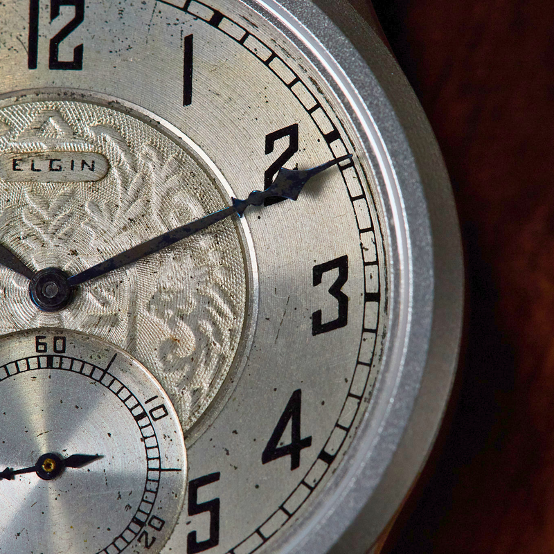 Close-up of an Elgin watch face with detailed engraving on a wooden surface