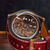 A close-up shot of a luxury watch with a transparent back, showcasing an intricate mechanical movement, resting on a dark wooden surface with a dark textured background.