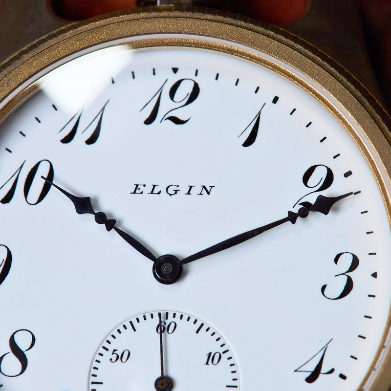Close-up of an Elgin pocket watch with a white face and gold casing.