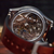 Close-up of a wristwatch with a transparent back showing a detailed mechanical movement, paired with a brown leather strap on a wooden surface.