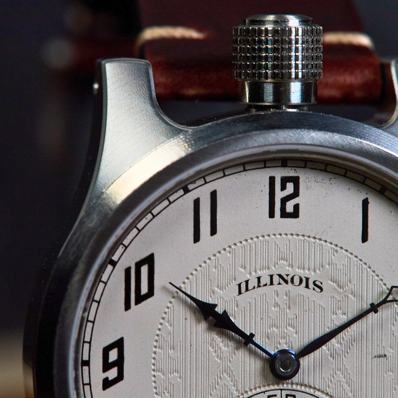 Close-up of a vintage-style wristwatch with a silver-toned metal case, a white dial featuring black Arabic numerals and hands, and a brown leather strap.