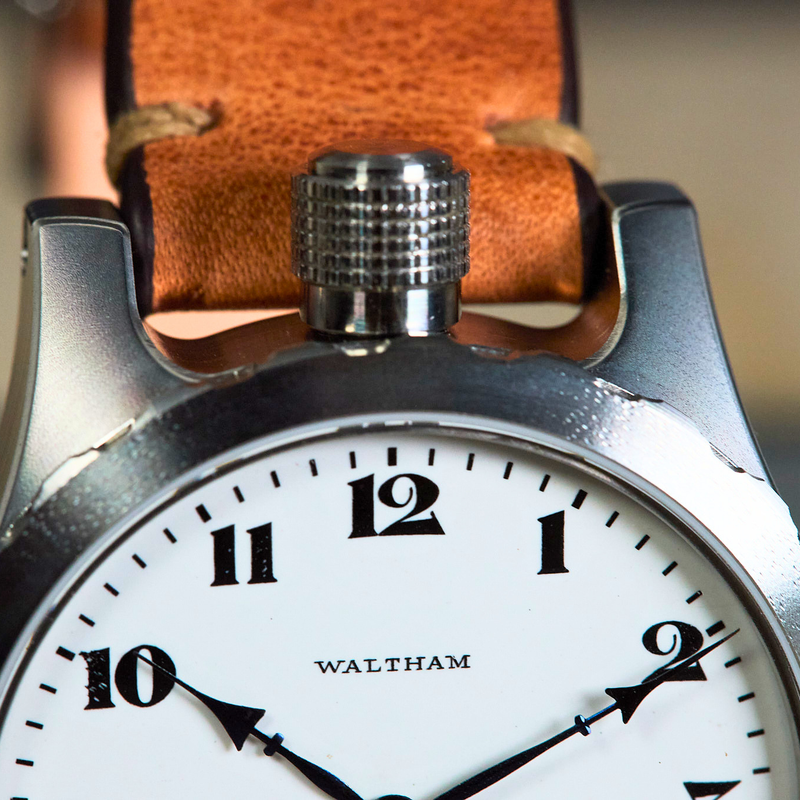 Close-up of a Waltham wristwatch with a silver-toned metal case, white dial, and brown leather strap.