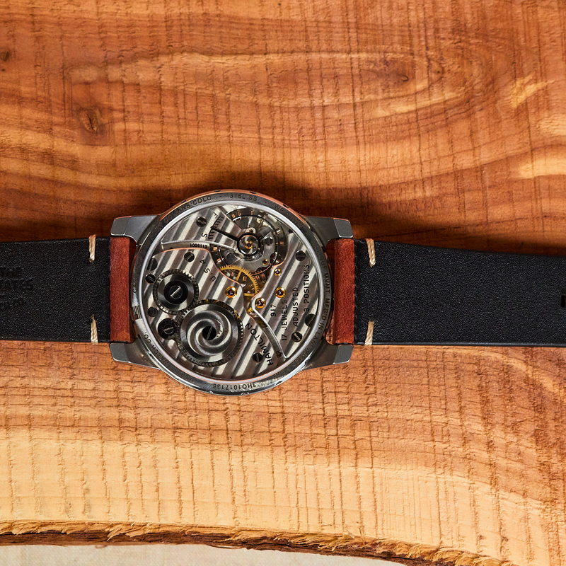 Watch with a black leather strap and visible mechanical components on a wooden surface