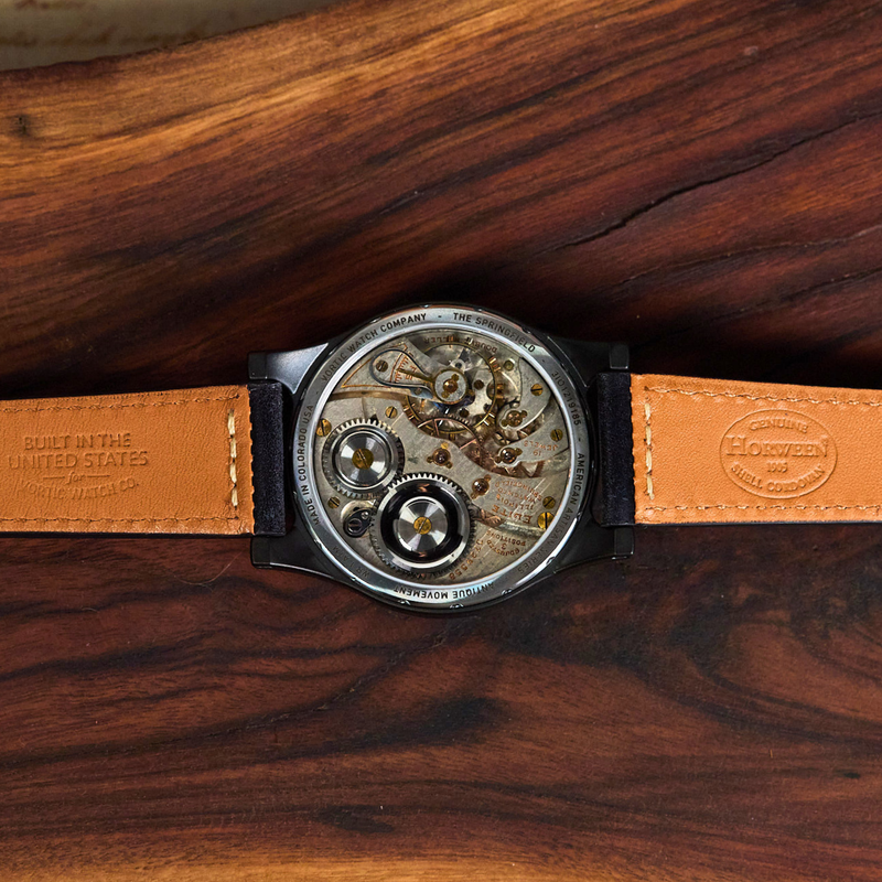 A vintage-style skeleton wristwatch with a tan leather strap and a detailed mechanical movement visible through the round case, laid flat on a dark wood surface.