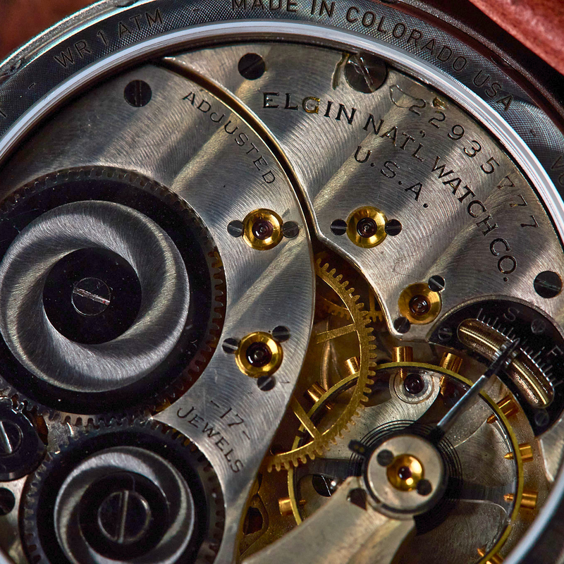 Close-up of a watch movement showing the back casing with engraved text including 'ELGIN NAIL WATCH CO.' and 'U.