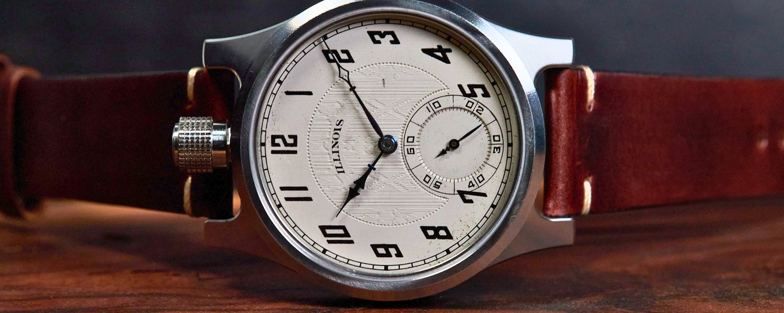 A close-up of a QUINCY watch with a silver-toned metal case, white dial, and brown leather strap, resting on a wooden surface against a dark background.